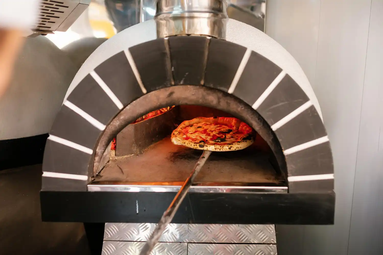 Forno de lastro sendo utilizado para assar uma pizza, destacando a tradição e eficiência desse tipo de forno em padarias e pizzarias.