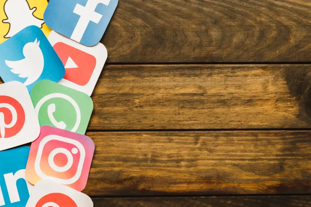 Conjunto de ícones de redes sociais como Facebook, Twitter, YouTube e Instagram sobre fundo de madeira, sugerindo como usar inteligência artificial para produzir conteúdo digital sem perder a qualidade.