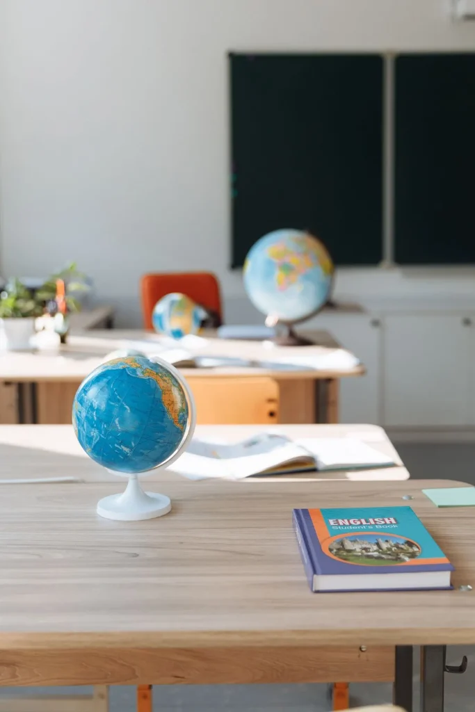 Sala de aula com globo terrestre e livro de inglês sobre a mesa, com ambiente educativo e lousa ao fundo; ideal para Escola de Inglês do Brasil: Guia Completo.