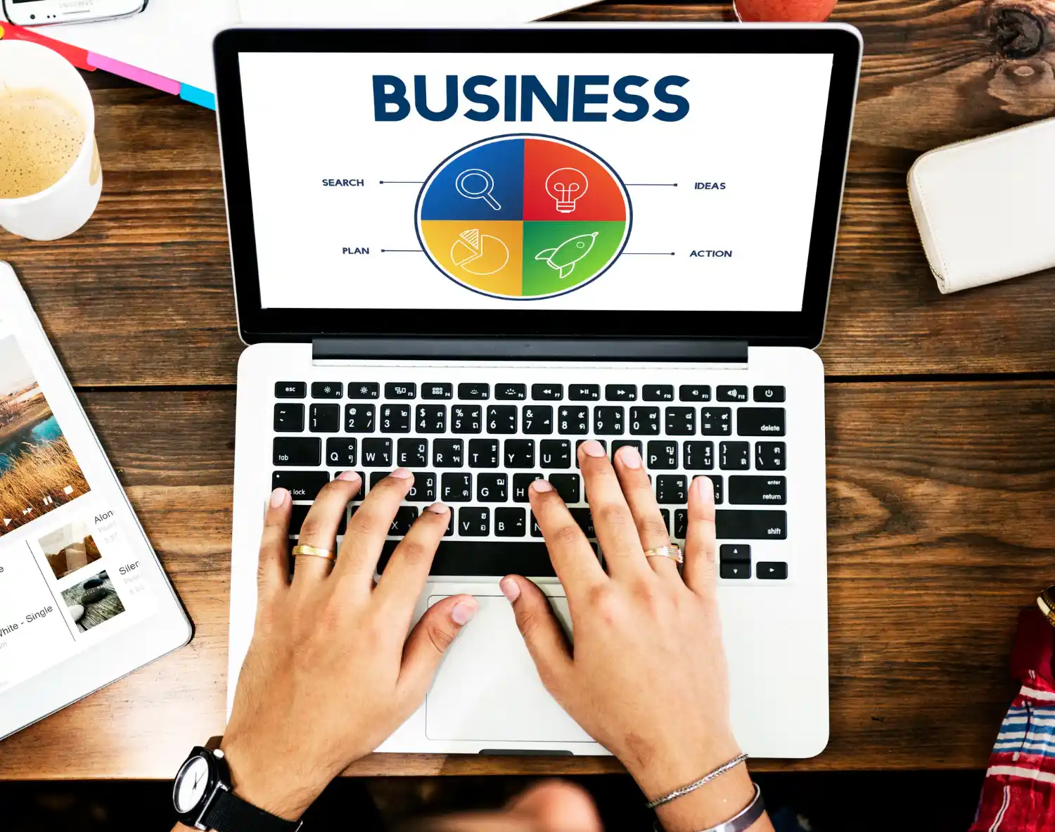 Marketing Digital para Pequenas Empresas: Como Criar uma Estratégia que Gera Resultados: Mesa de trabalho com notebook aberto exibindo o título “BUSINESS” e um painel de busca, ideias, planos e ação, enquanto mãos digitam no teclado; cenário de marketing e planejamento digital.
